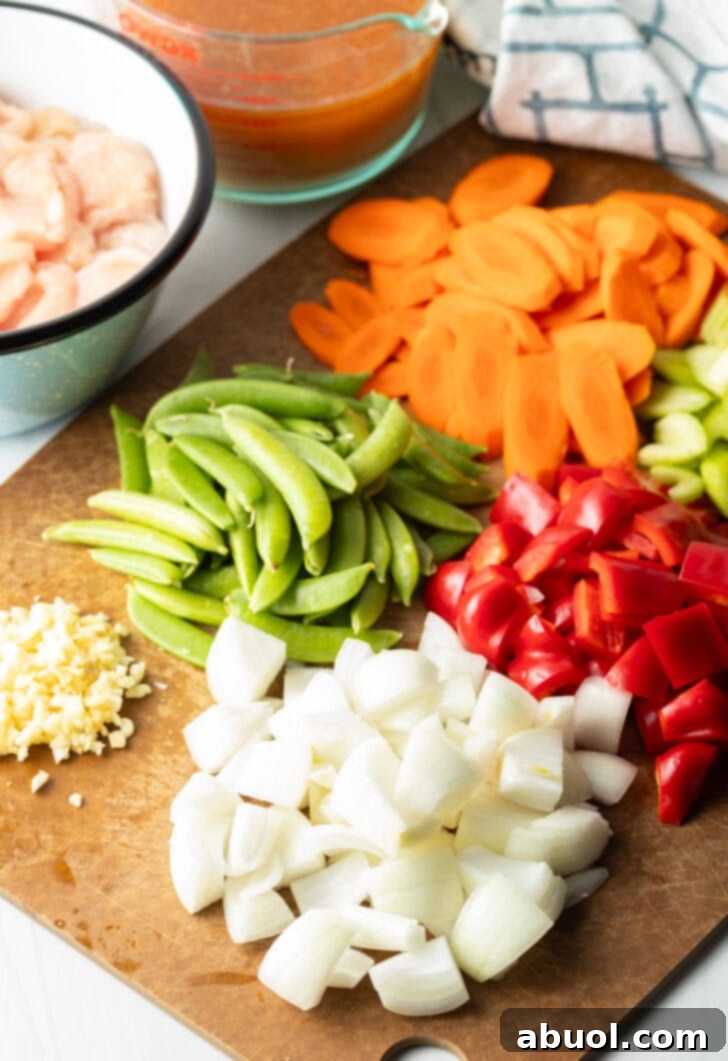Recipe ingredients on a cutting board. Piles of chopped carrots, red bell pepper, onion, garlic, and snap peas.