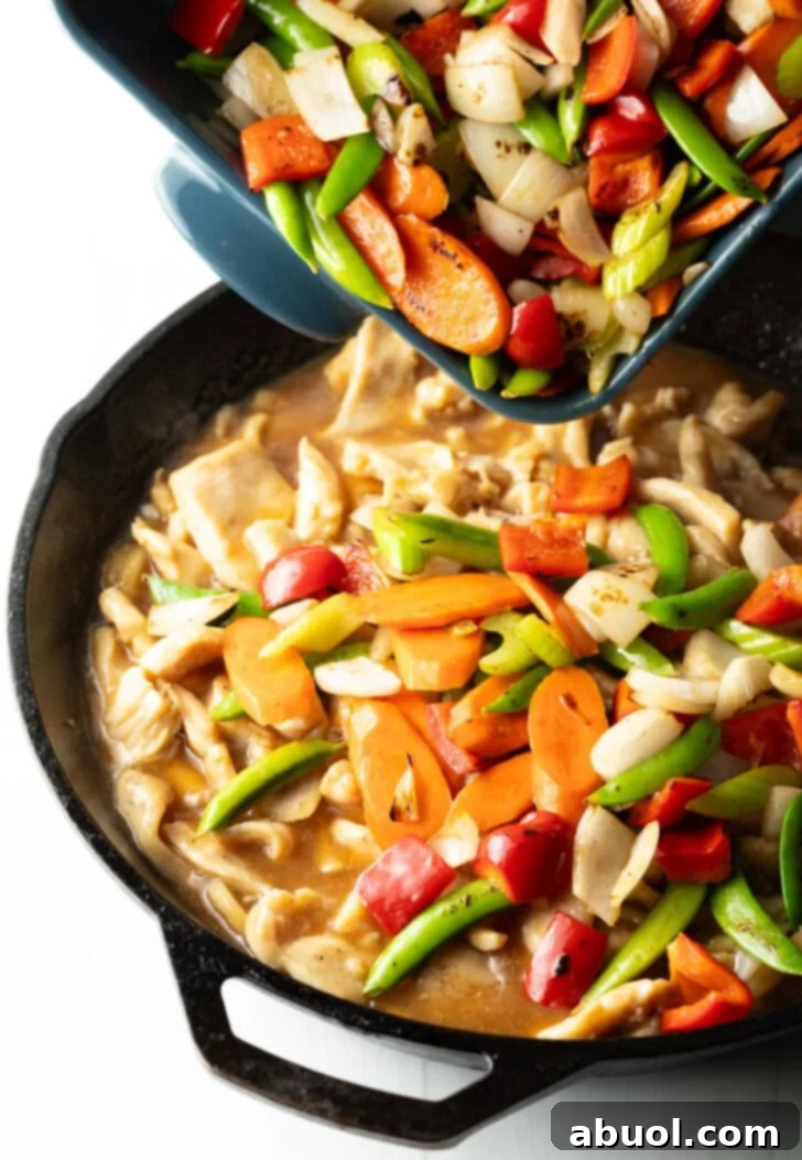 Adding vegetables to cast iron skillet with chicken pieces.