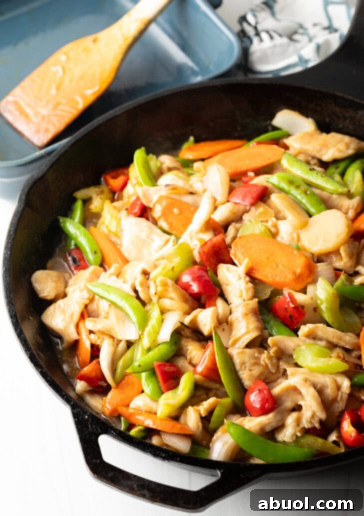 Cast iron skillet with cooked pieces of chicken, snap peas, red bell pepper, carrot slices, chopped onion, and minced garlic.