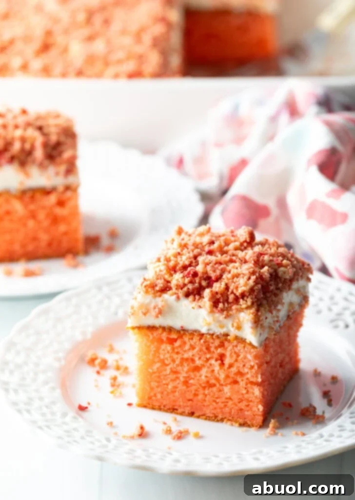 Berry Crumble Bliss Cake 2 A perfectly cut square of strawberry crunch cake, showcasing its delicate pink interior, creamy white frosting, and crunchy crumble topping, resting elegantly on a pristine white plate.