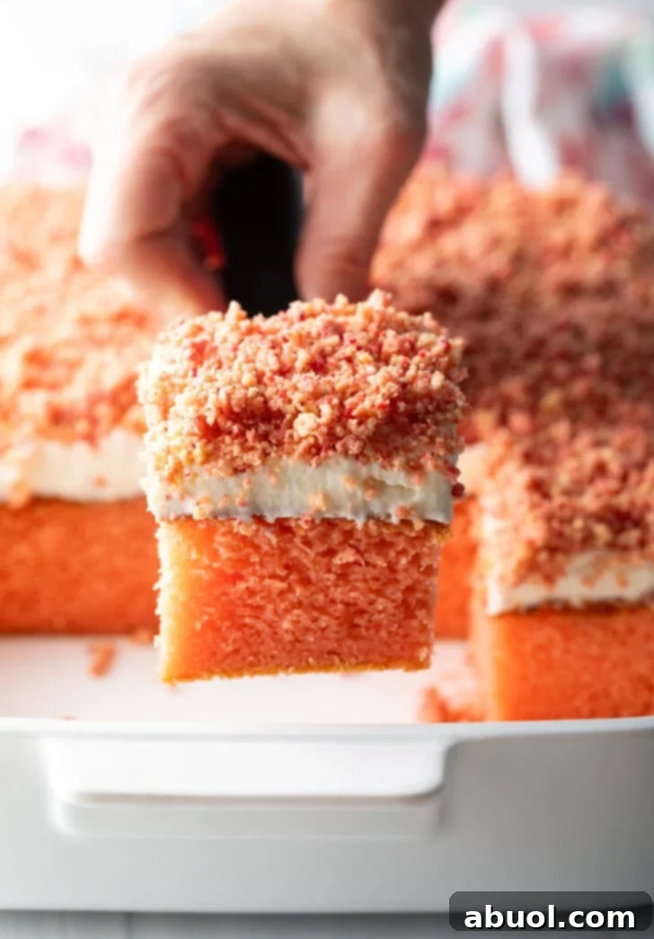 Berry Crumble Bliss Cake 14 A delectable baked strawberry crunch cake with a generous layer of crumble topping. A portion has been expertly removed, revealing the fluffy, soft pink cake interior beneath a luscious white frosting. A metal spatula is poised, ready to serve another perfect square.