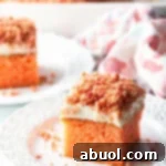 A perfectly cut square of strawberry crunch cake, showcasing its delicate pink interior, creamy white frosting, and crunchy crumble topping, resting elegantly on a pristine white plate.
