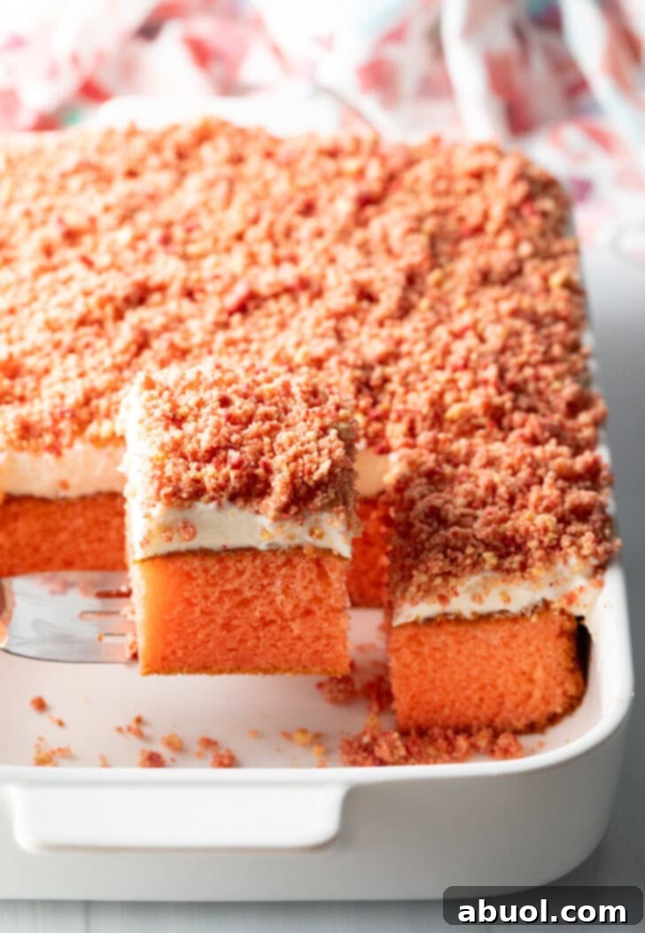 Berry Crumble Bliss Cake 4 A delectable baked strawberry crunch cake with a generous layer of crumble topping. A portion has been expertly removed, revealing the fluffy, soft pink cake interior beneath a luscious white frosting. A metal spatula is poised, ready to serve another perfect square.