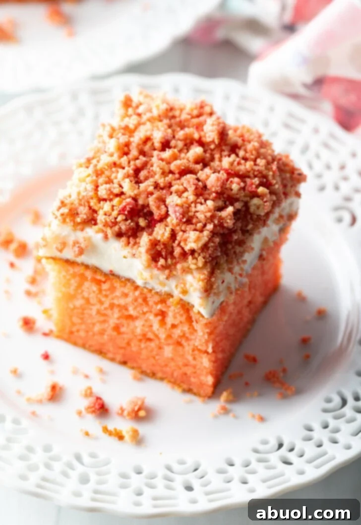 Berry Crumble Bliss Cake 5 A perfectly cut square of strawberry crunch cake, showcasing its delicate pink interior, creamy white frosting, and crunchy crumble topping, resting elegantly on a pristine white plate.