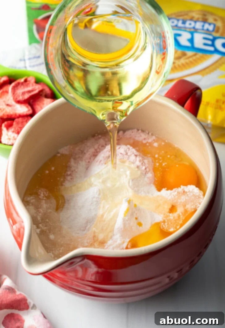 Berry Crumble Bliss Cake 7 A measuring cup carefully pouring vegetable oil into a vibrant red mixing bowl, joining other cake ingredients to create a smooth batter.