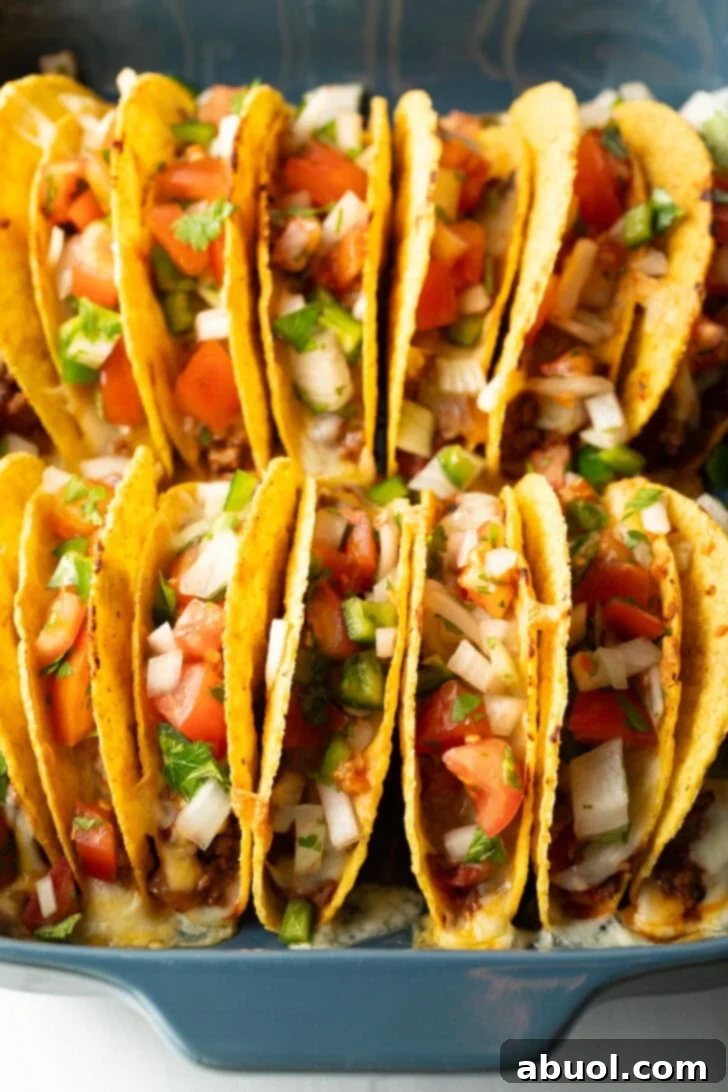 Two rows of a dozen loaded yellow corn hard shell tacos, standing upright in a large baking dish.