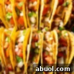 Two rows of a dozen loaded yellow corn hard shell tacos, standing upright in a large baking dish.