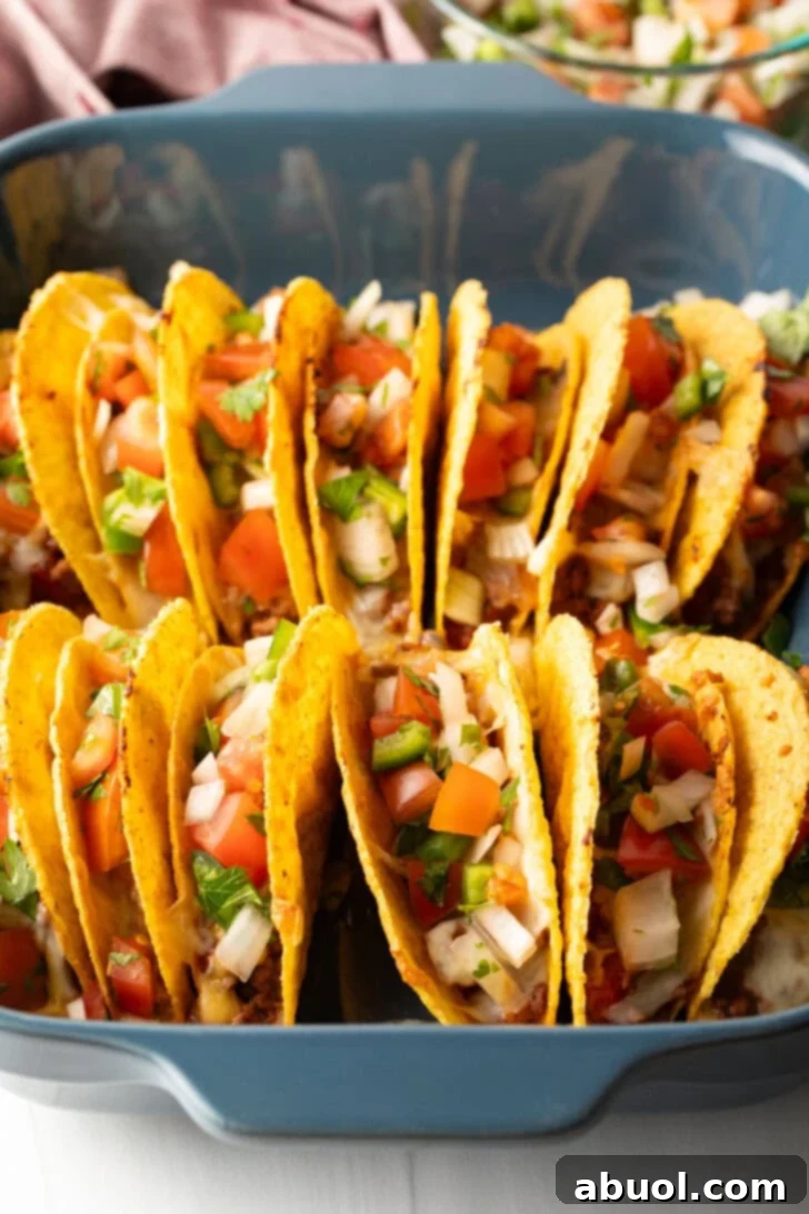 Two rows of a dozen loaded yellow corn hard shell tacos, standing upright in a large baking dish.