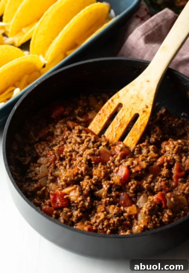 Wooden spatula stirring ground beef taco mixture in a large black deep skillet.