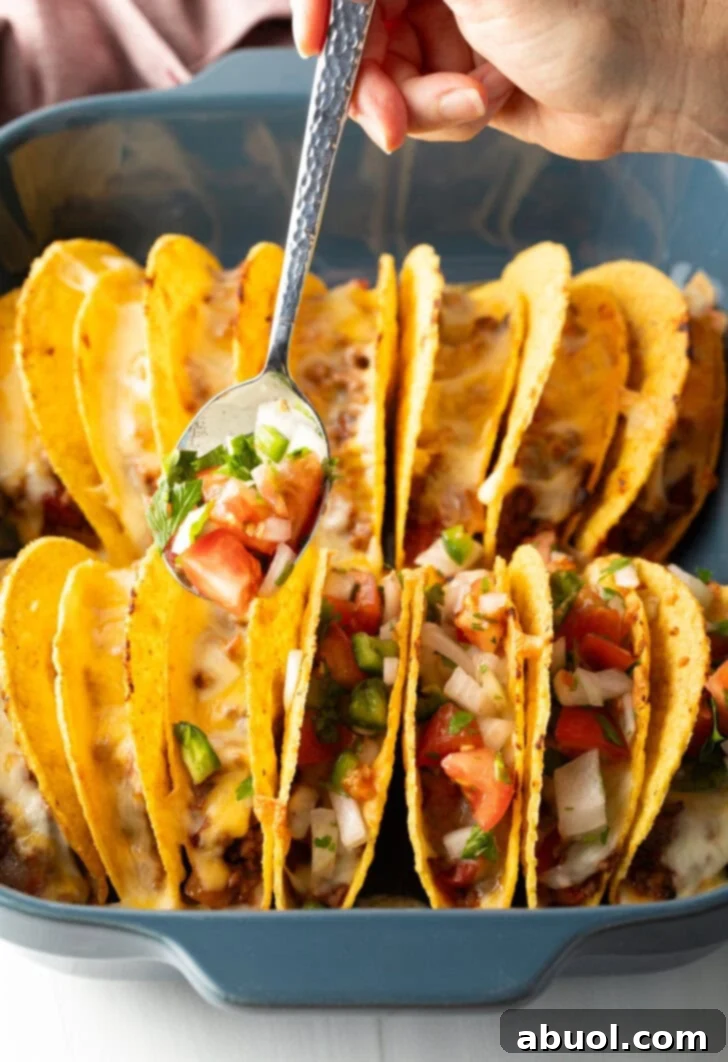 Spoon adding pico de gallo to a row of hard shell tacos.
