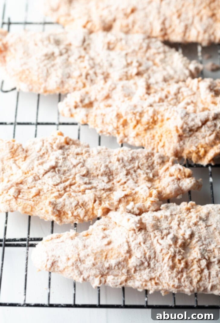 Blazing Honey Chicken 7 Five perfectly breaded and thin chicken breast cutlets neatly arranged on a wire rack, ready for frying. The visible texture of the coating promises a satisfying crunch.