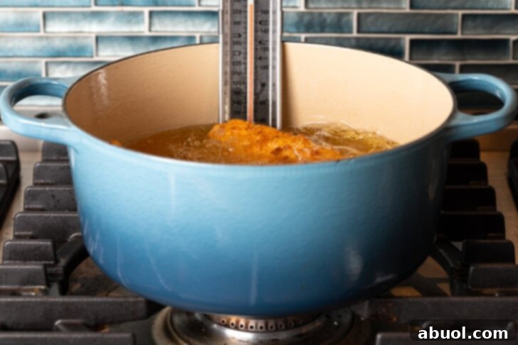 Blazing Honey Chicken 8 A vibrant blue cooking pot filled with hot oil, in which several pieces of chicken are actively frying. A clip-on thermometer is clearly visible on the pot's side, indicating precise temperature monitoring during the frying process.