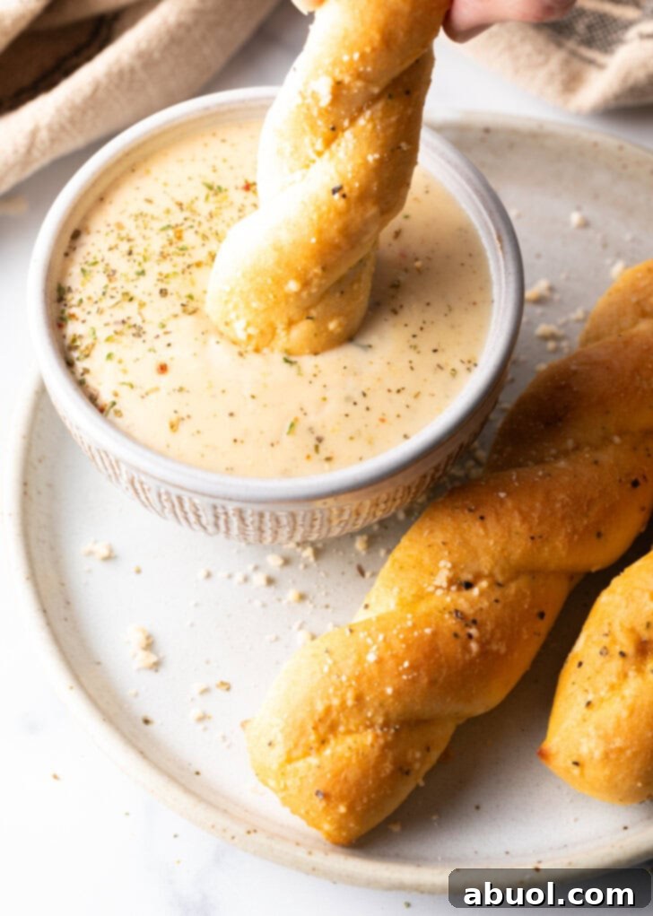Top down view of a breadstick being dipped into a ramekin of creamy garlic sauce.