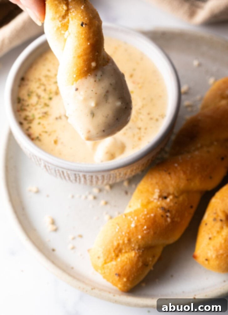 Top down view of a breadstick being dipped into a ramekin of creamy garlic sauce.