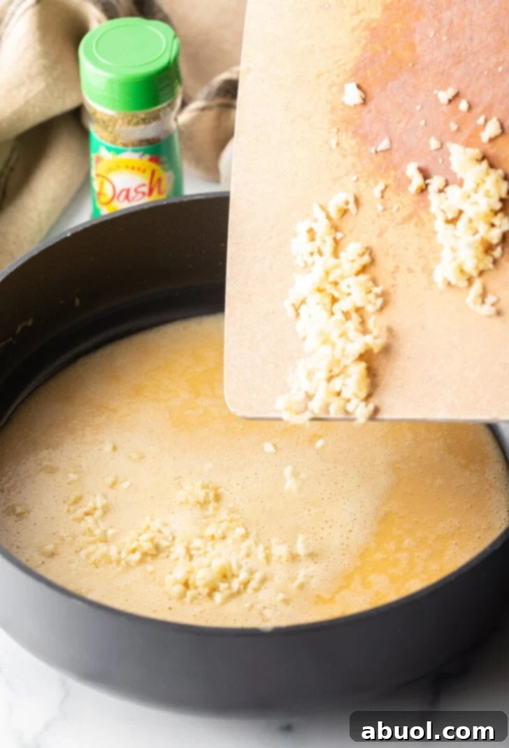 Adding minced garlic from a cutting board into a skillet with sauce roux.