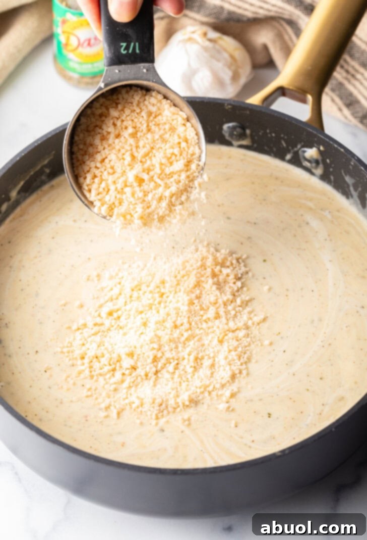 Adding grated parmesan cheese from a measuring cup into the skillet.