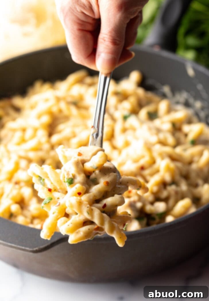 Hand holding forkful of pasta to camera.