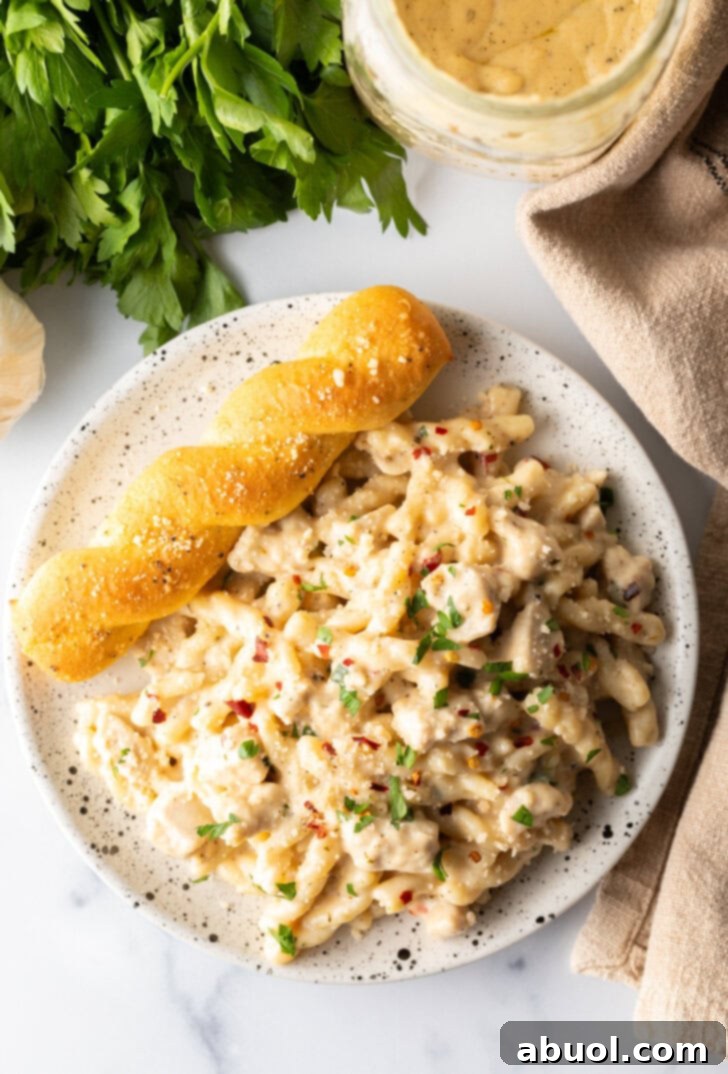 Top down view of white plate of cheesy garlic parmesan chicken pasta with a breadstick twist on the side of the plate