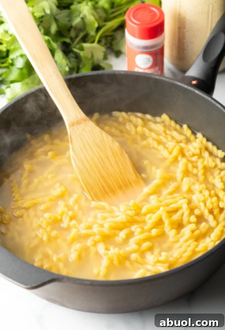 Wood spatula stir past and broth in a deep skillet.