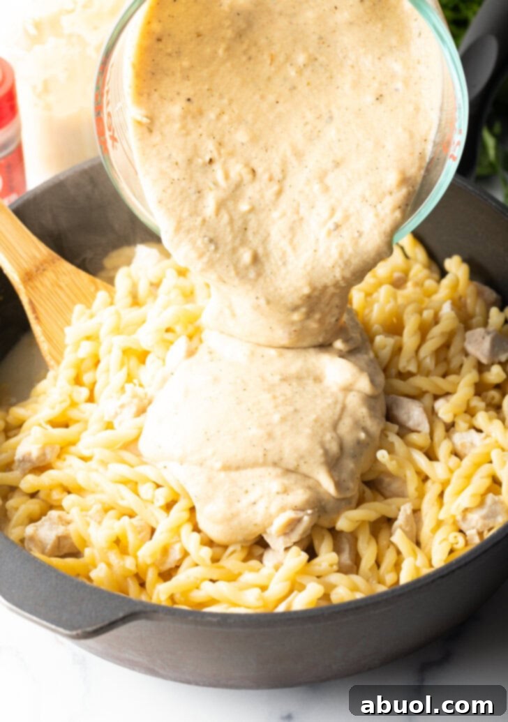Adding parmesan cream sauce to the pasta in a pot.