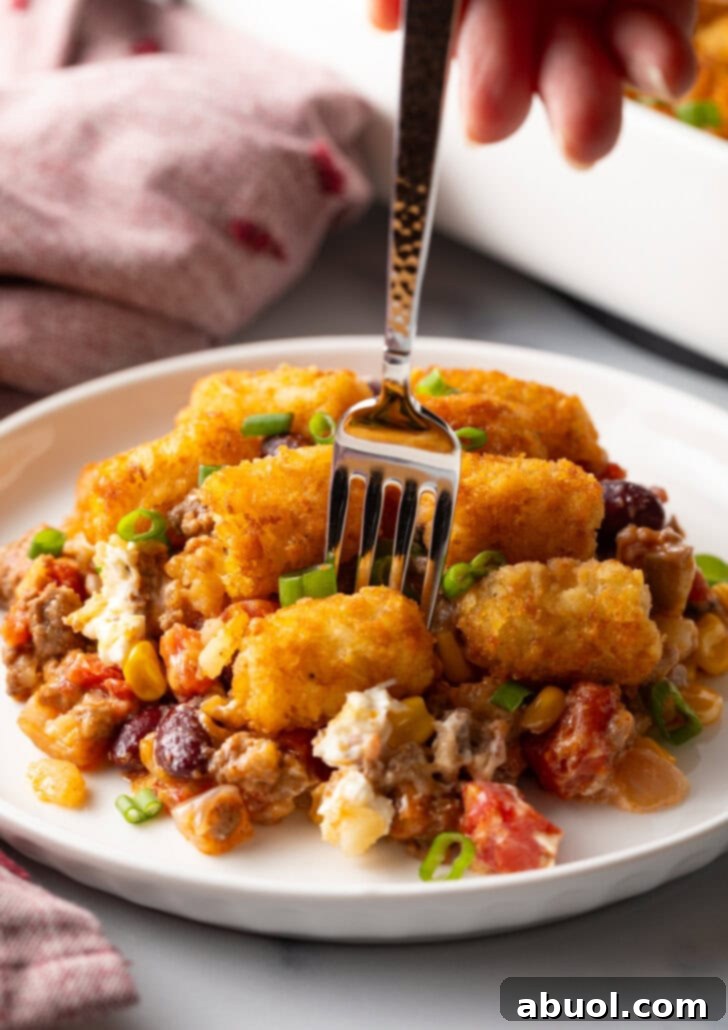 White plate with tater tot and ground beef cowboy casserole. A fork is taking a bite from the plate.