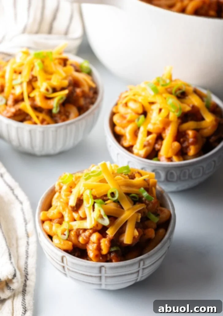 Hearty Beef and Macaroni Skillet 3 Three vibrant bowls of homemade beefaroni, garnished with fresh shredded cheddar cheese and finely chopped scallions, ready for serving.