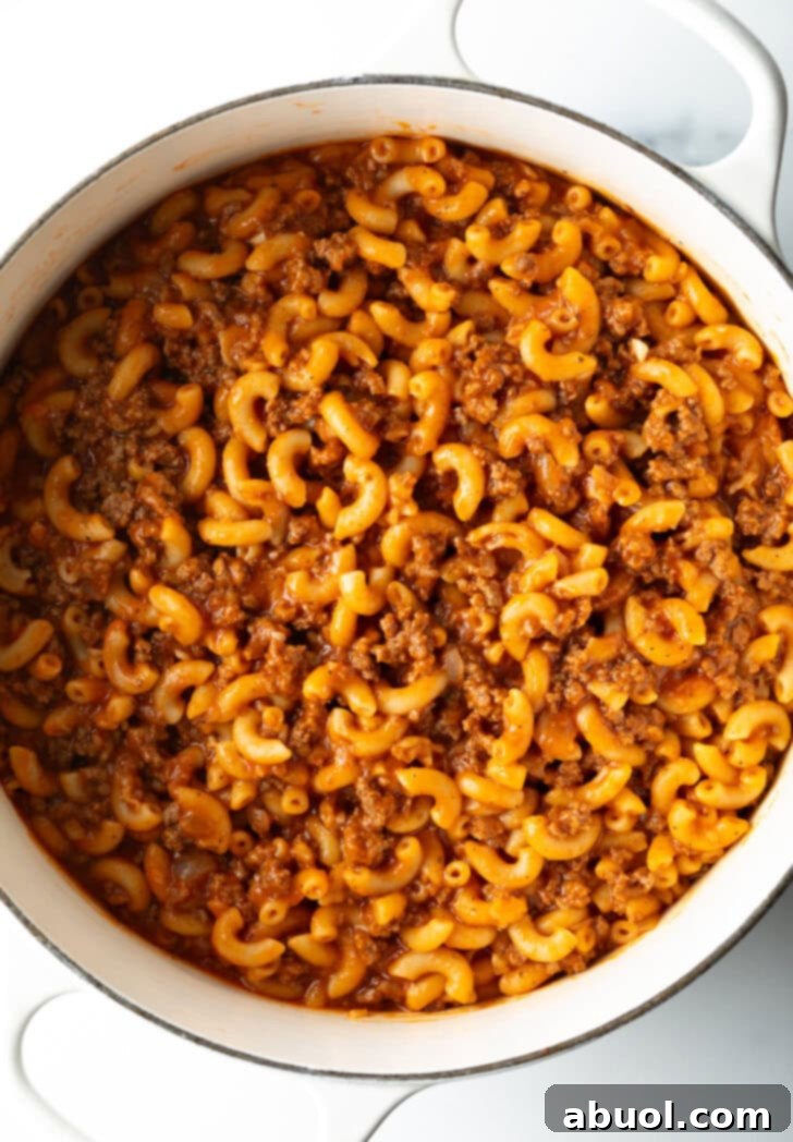 Hearty Beef and Macaroni Skillet 7 Top-down view of homemade beefaroni simmering in a large cooking pot, with the sauce thickening around the macaroni and ground beef.