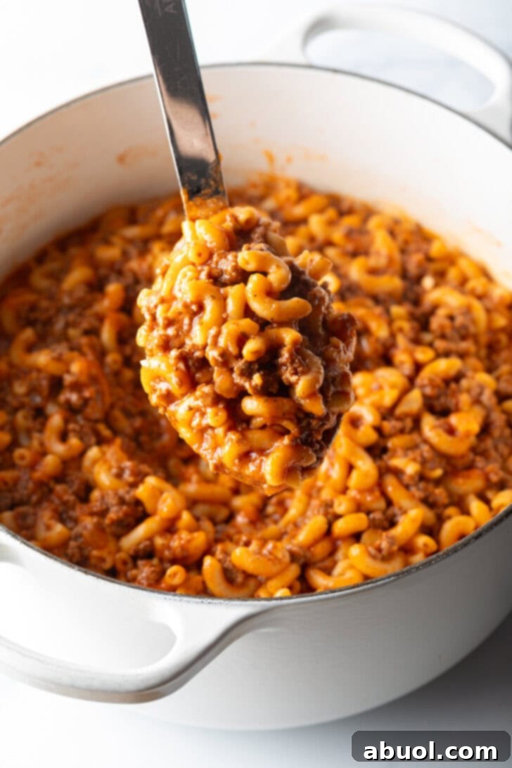 Hearty Beef and Macaroni Skillet 8 A large metal spoon lifting a generous serving of homemade beefaroni from the pot, showcasing the rich sauce, macaroni, and ground beef.