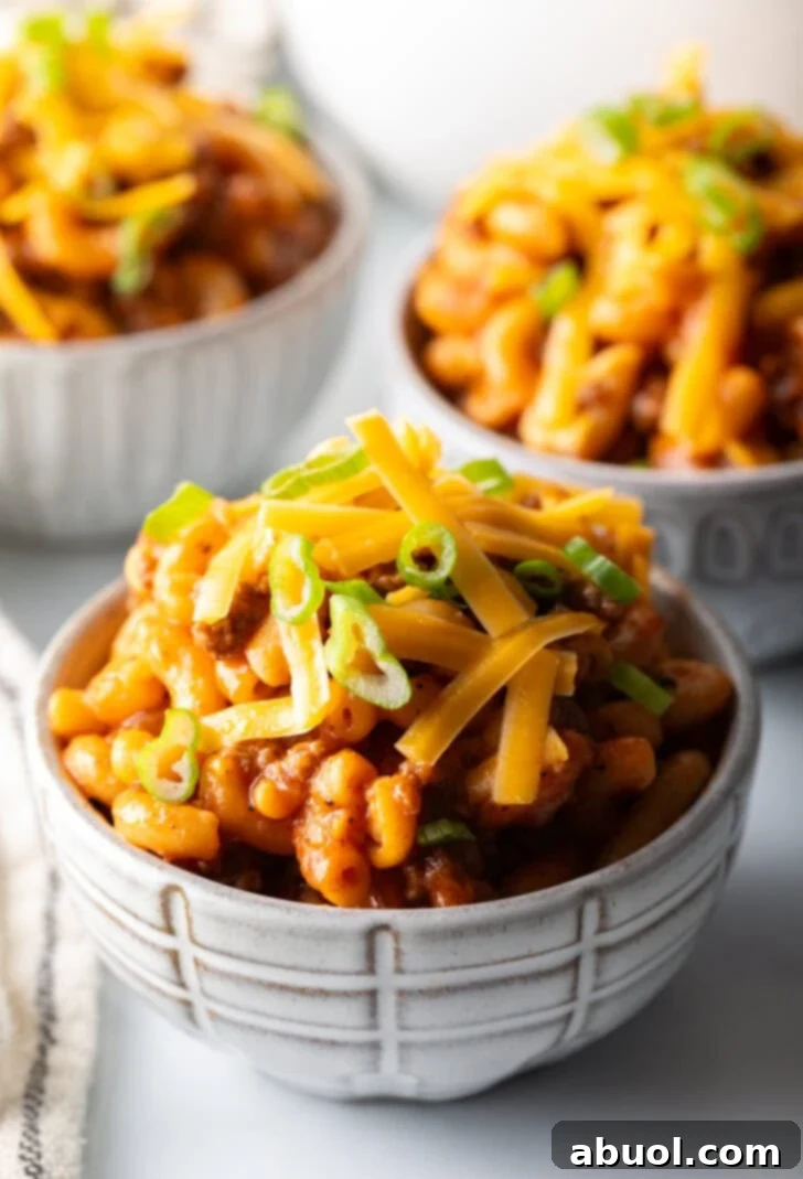 Hearty Beef and Macaroni Skillet 10 A single bowl of homemade beefaroni, generously topped with shredded cheddar cheese and chopped green onions, set against a blurred background.