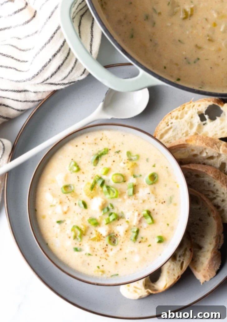 An overhead view of a steaming bowl of homemade fish chowder, garnished with parsley, served on a plate with bread slices.