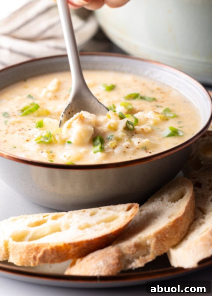 A close-up side view of a spoon dipping into a creamy fish chowder, revealing tender fish and potato chunks.