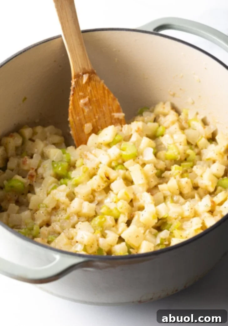 Chopped onion, celery, and potato cooking in a large pot with a wooden spatula, forming the base of the fish chowder.