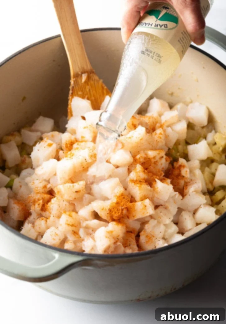 A stream of clam juice being poured into a large pot containing chopped seafood and vegetables for the chowder.