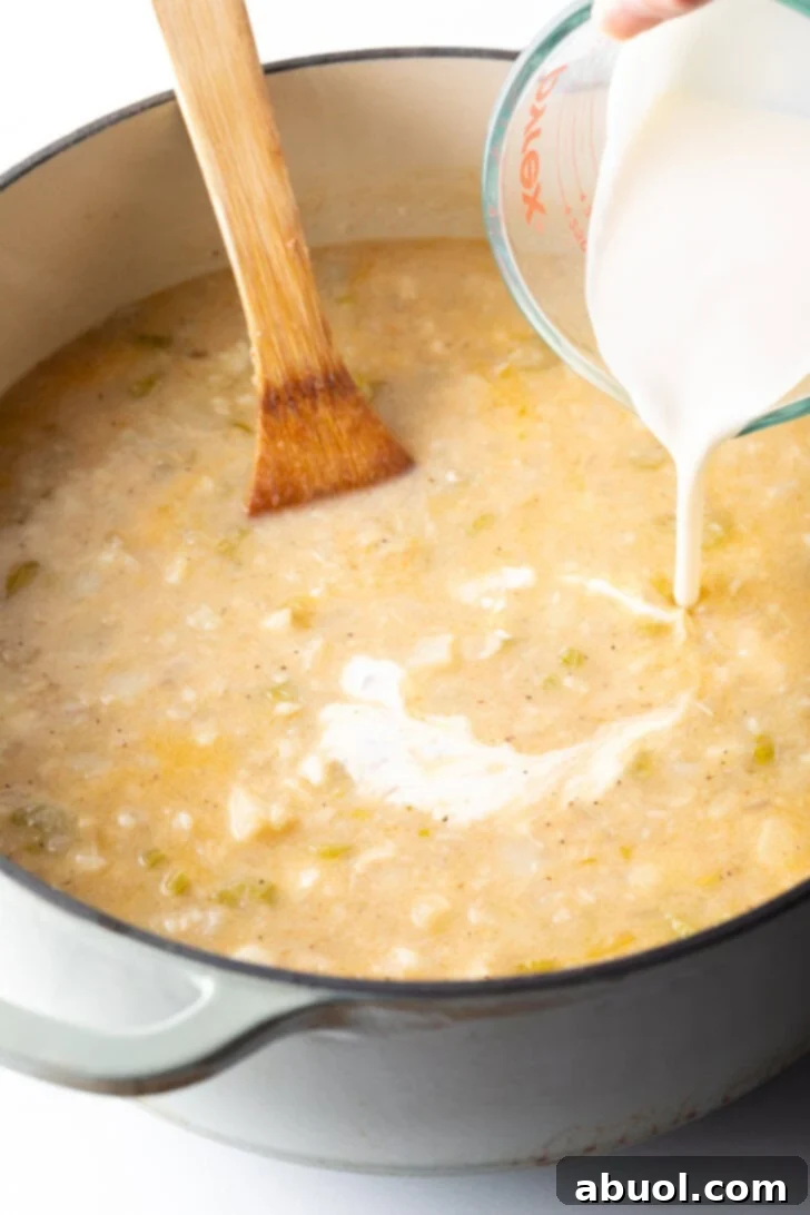 Heavy cream being poured into the simmering soup base in a large pot, adding richness to the chowder.