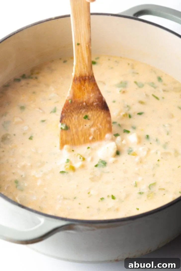 A wooden spatula gently stirring the creamy fish chowder in a large cooking pot, mixing in the last ingredients.