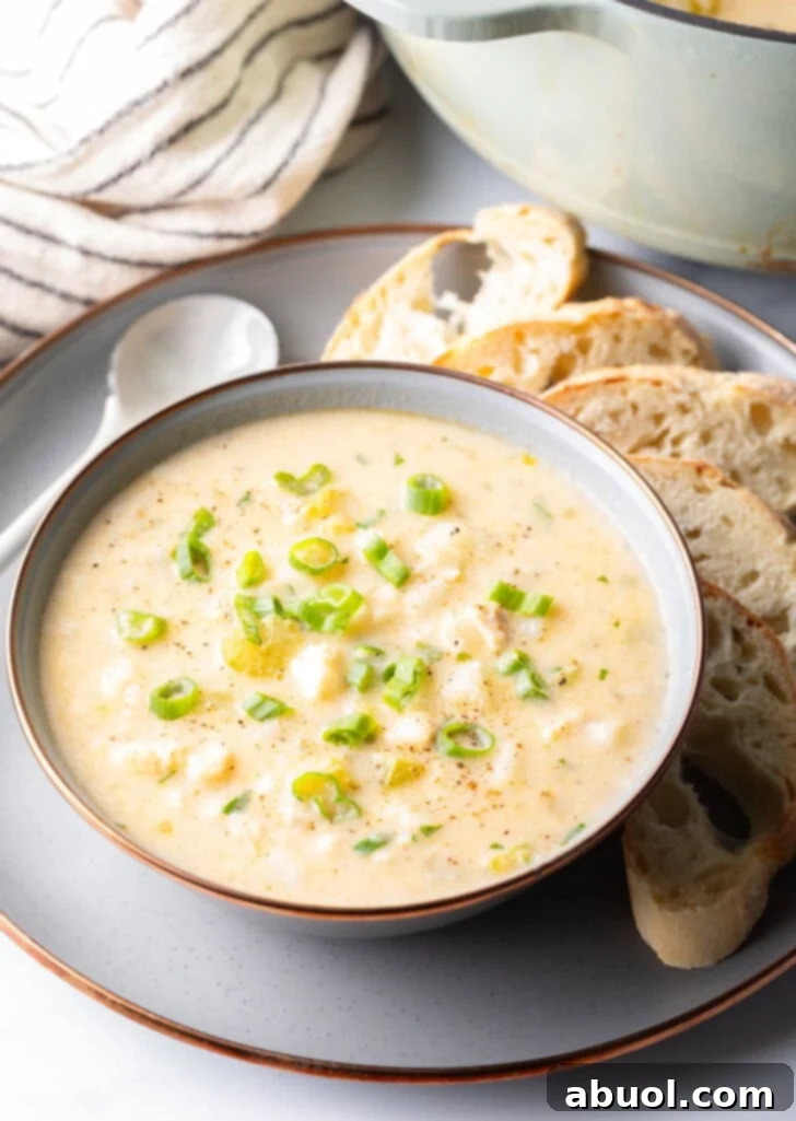 A beautifully presented bowl of creamy fish chowder, accompanied by slices of bread and a spoon, ready to be enjoyed.