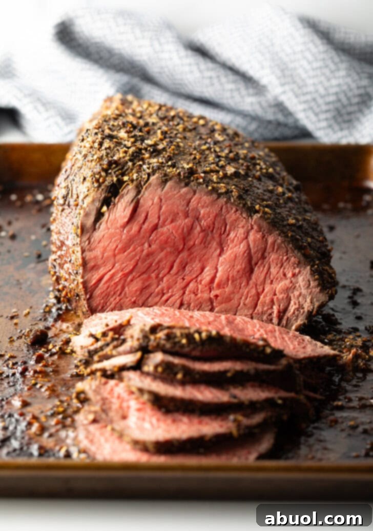 Classic Family Roast Beef 2 Cooked beef top round roast on a metal baking pan. The front half of the roast has been thinly sliced.