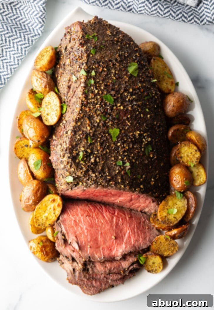 Classic Family Roast Beef 11 Cooked beef round roast on a metal baking pan. The front half of the roast has been thinly sliced and the meat is surrounded by roasted baby potatoes.