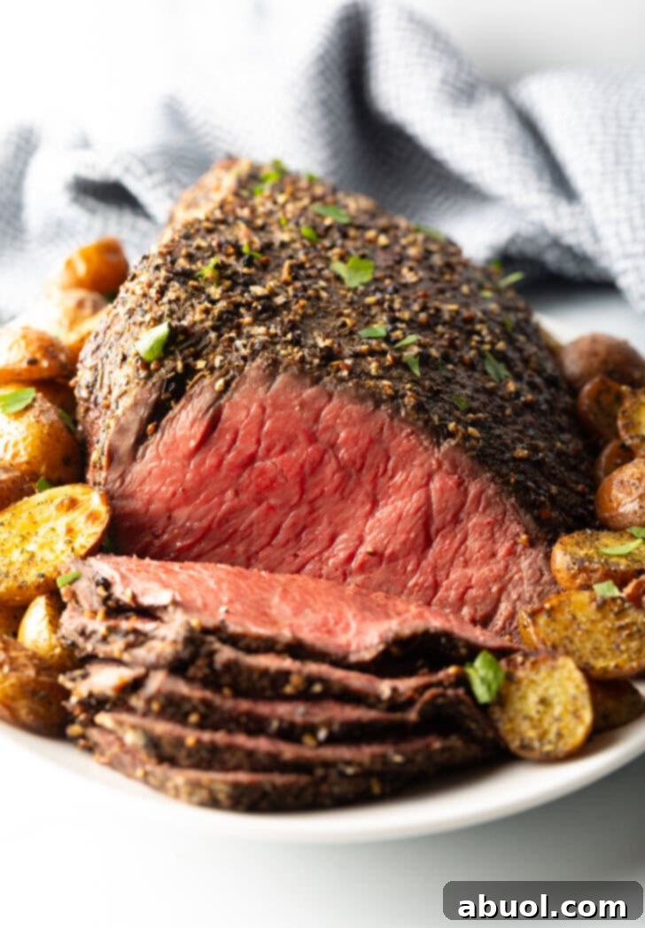 Classic Family Roast Beef 12 Cooked beef round roast on a metal baking pan. The front half of the roast has been thinly sliced and the meat is surrounded by roasted baby potatoes.