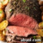 Classic Family Roast Beef 13 Cooked beef round roast on a metal baking pan. The front half of the roast has been thinly sliced and the meat is surrounded by roasted baby potatoes.