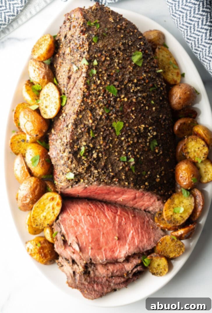 Classic Family Roast Beef 4 Cooked beef round roast on a metal baking pan. The front half of the roast has been thinly sliced and the meat is surrounded by roasted baby potatoes.