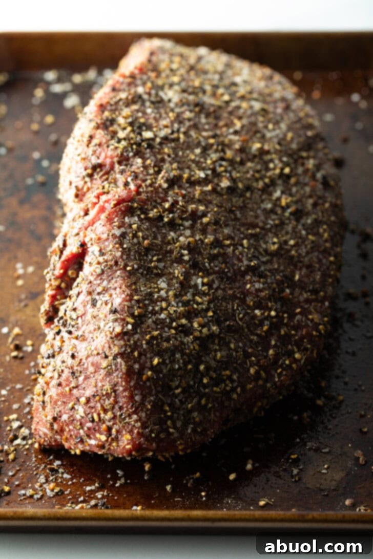 Classic Family Roast Beef 8 Raw top round roast coated with pepper rub, on a baking sheet.