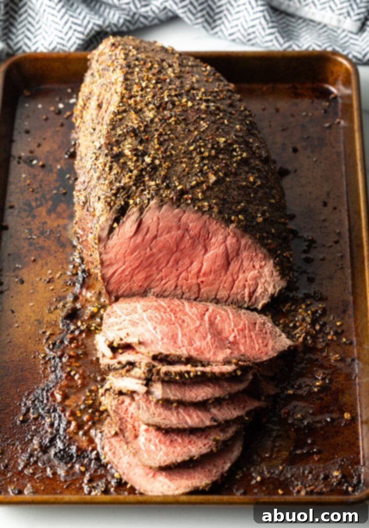 Classic Family Roast Beef 10 Top down view cooked beef top round roast on a metal baking pan. The front half of the roast has been thinly sliced.