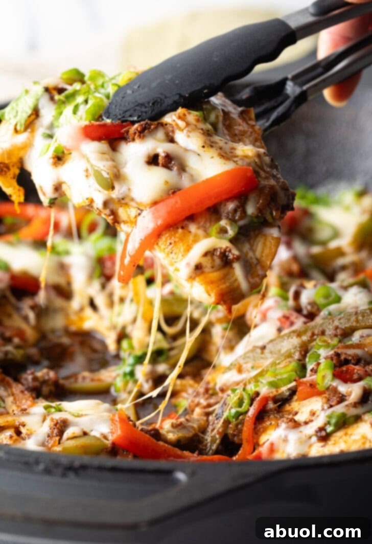 Choripollo in a black skillet, topped with cheese and green onions. A hand with tongs is taking a bit of the peppers and chicken.