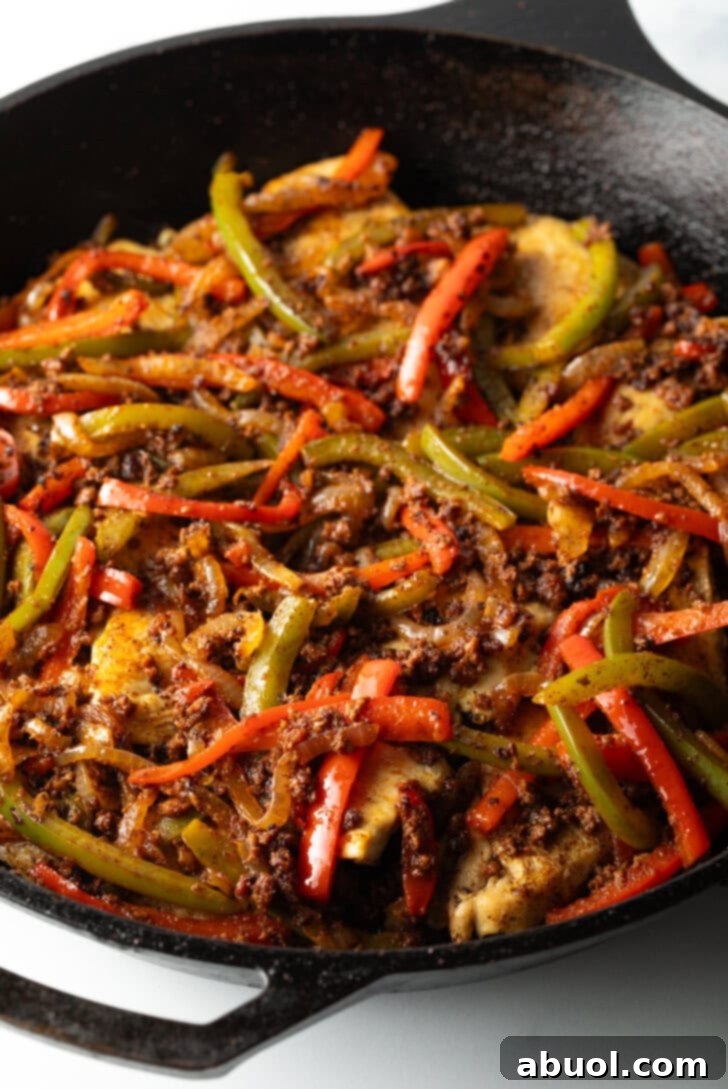 Yellow, green, orange, and red sliced bell peppers in a black skillet with seasonings.