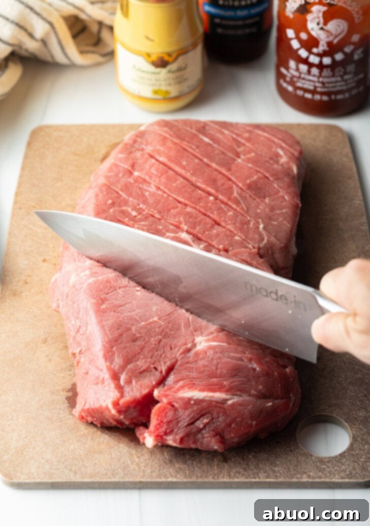 Knife scoring a large section of London broil on a cutting board with a criss-cross diagonal pattern.