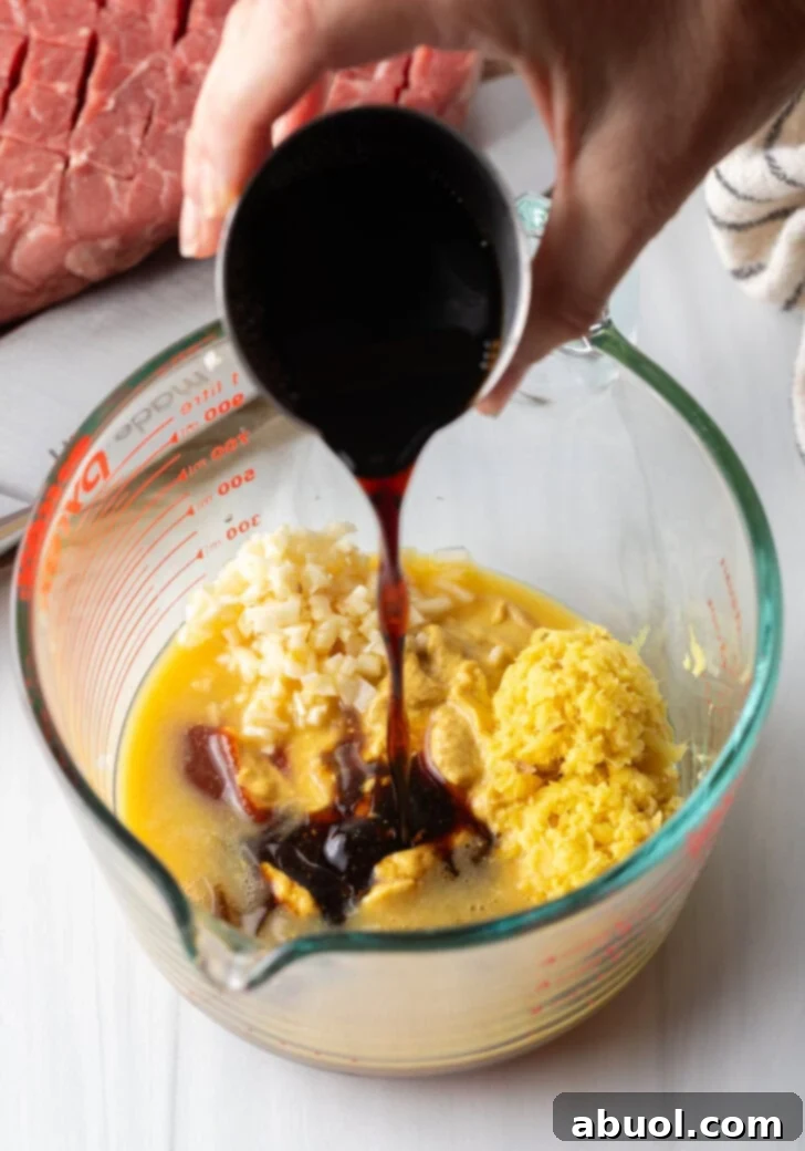 Hand adding dark brown sauce to glass measuring cup with marinade ingredients.