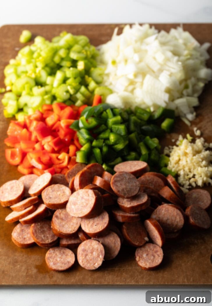 Louisiana Classic Gumbo 4 Prepped gumbo ingredients laid out on a wooden cutting board: Sliced andouille sausage, diced red and green bell peppers, chopped onion, celery, and minced garlic.