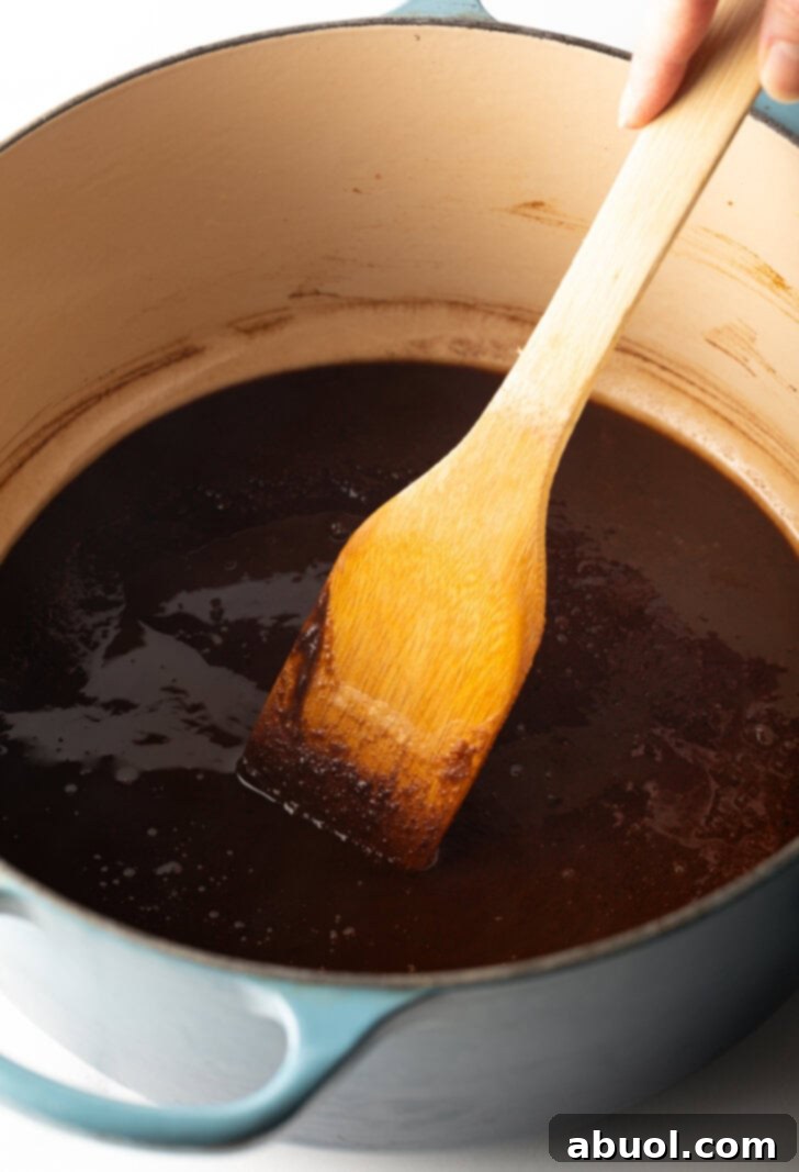 Louisiana Classic Gumbo 5 A wooden spatula actively stirring a dark, rich brown roux in a large cooking pot, demonstrating the essential step for gumbo preparation.
