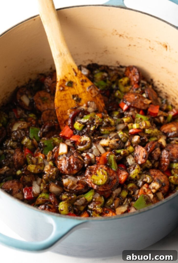 Louisiana Classic Gumbo 6 A wooden spatula stirring diced bell peppers, onions, and celery in a large pot, mixed with the dark roux, beginning to soften.
